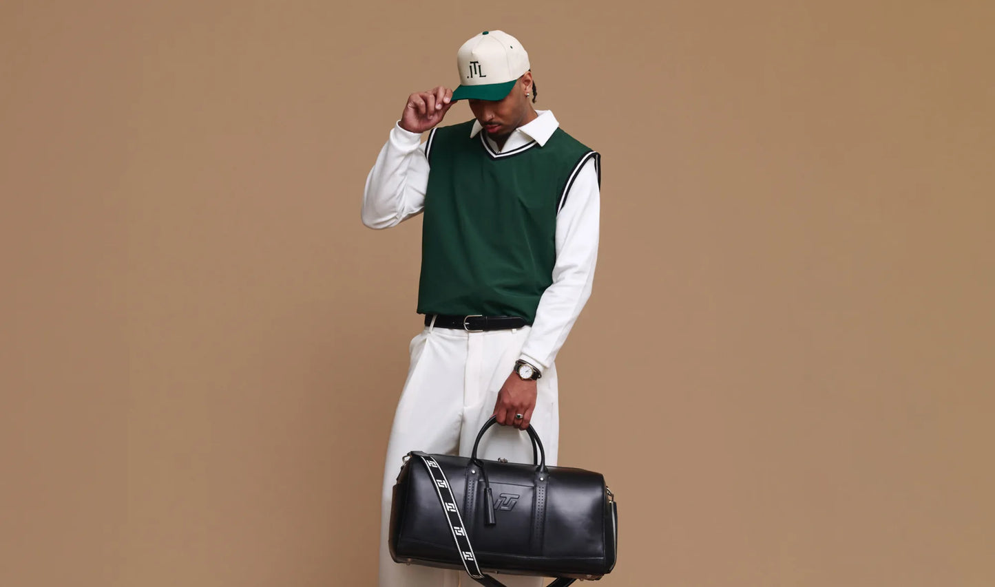 Man holding a black duffel bag against a beige background