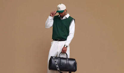 Man holding a black duffel bag against a beige background