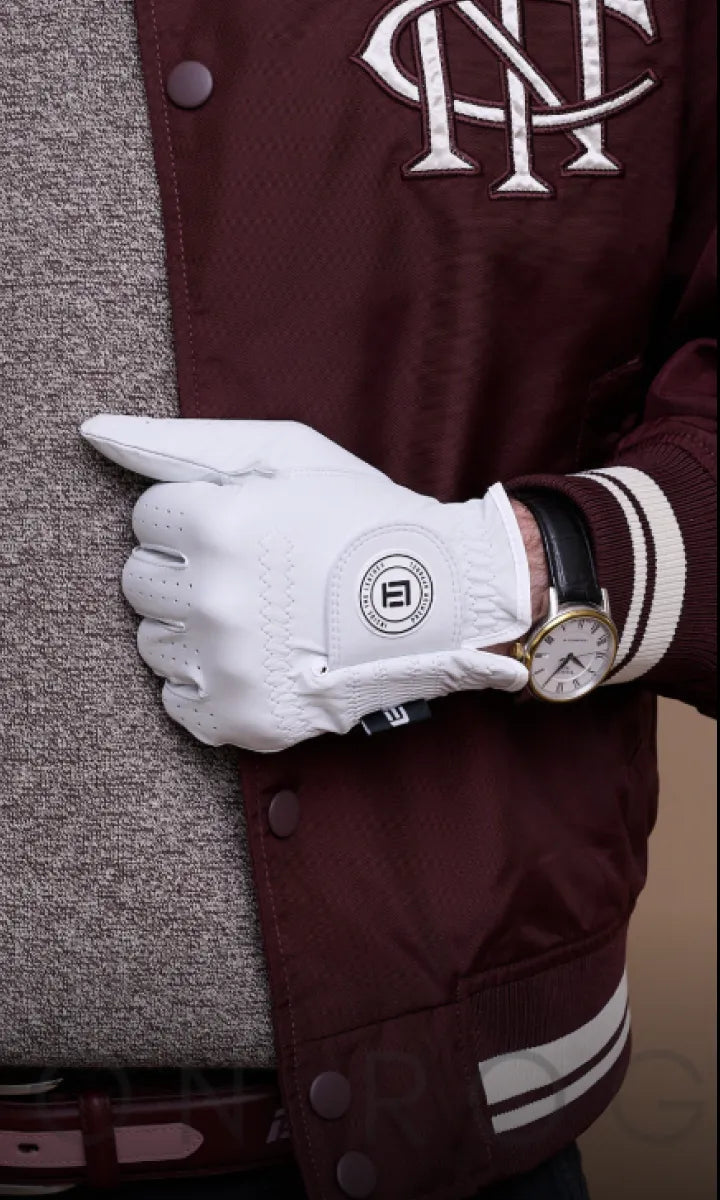White golf glove held by a person wearing a maroon jacket with a logo.