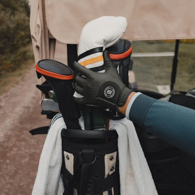 Person holding a golf club head cover with a glove on a blurred golf course background