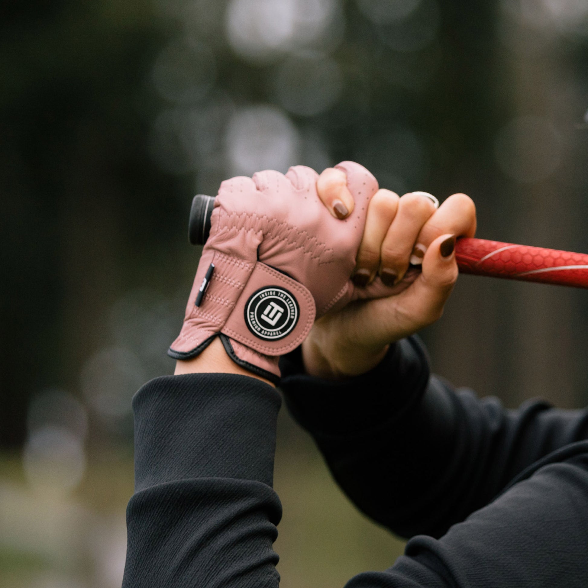 Hand wearing a pink golf glove holding a golf club with a blurred natural background